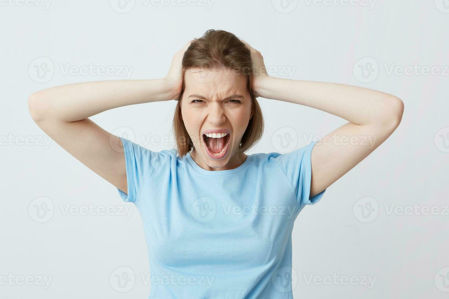 Closeup of mad annoyed young woman in blue t shirt with hand on head feels angry and shouting isolated over white background Looks crazy photo