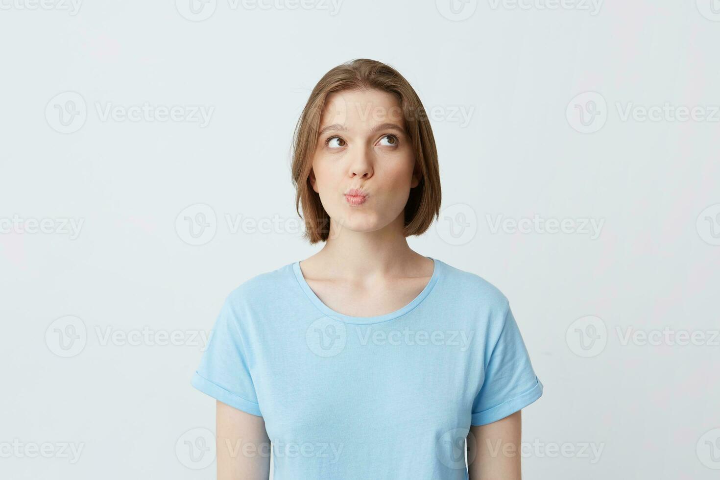 Portrait of pensive pretty young woman in blue t shirt thinking and feels puzzled isolated over white background Looks to the side nd frowning her face photo