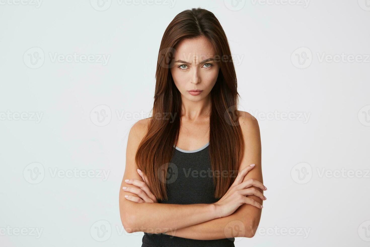 Closeup of angry displeased young woman standing with hands folded and feels irritated isolated over white background Looks directly in camera photo