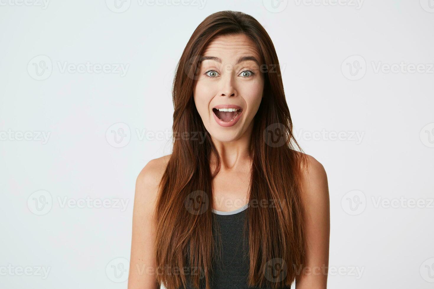 Happy excited young woman with long hair standing with opened mouth and looks surprised isolated over white background photo