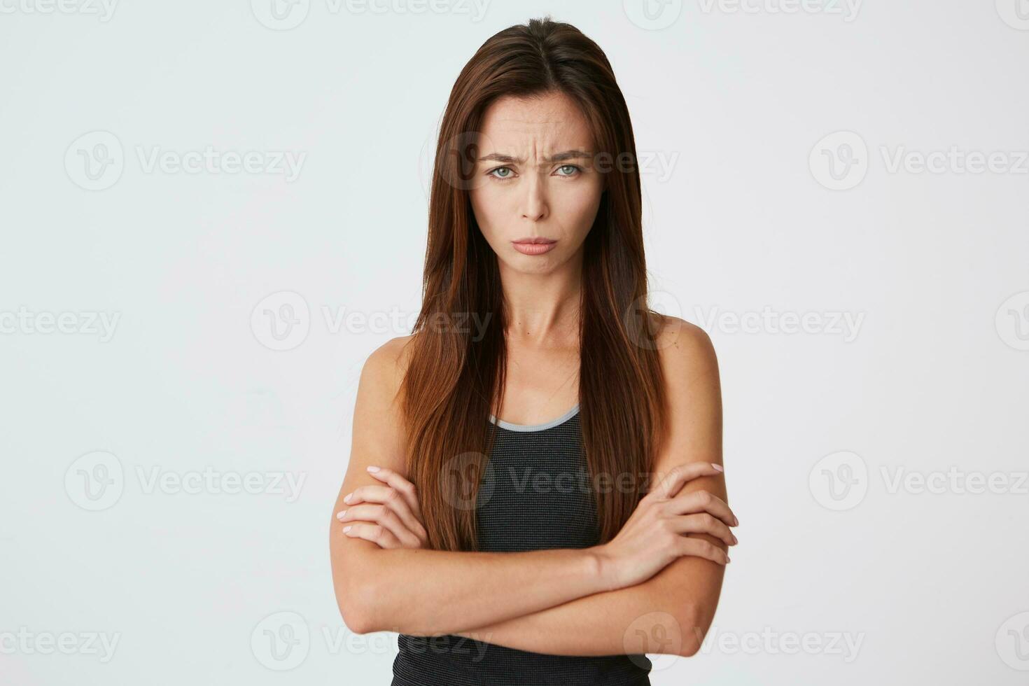 Sad upset young woman with long hair standing with arms crossed and looking offended isolated over white background Feels disappointed photo