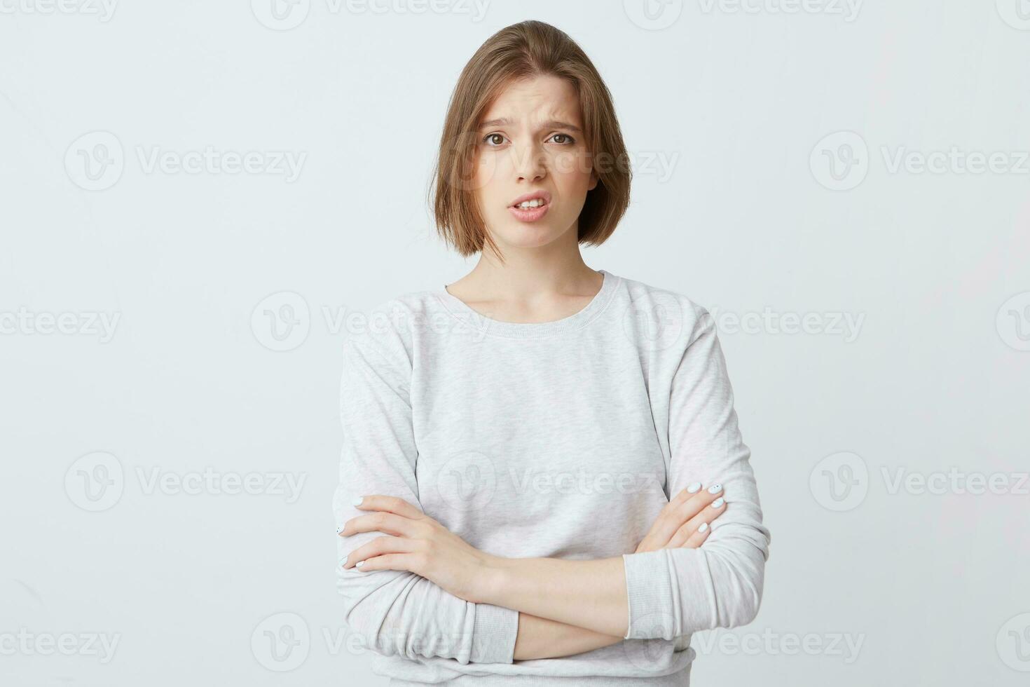 Portrait of upset disappointed young woman in long-sleeve standing with arms crossed and looks dissatisfied isolated over white background photo