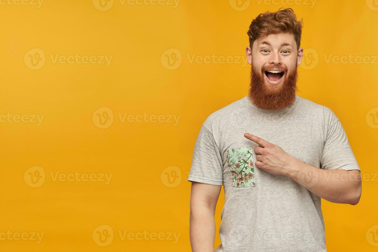 indoor shot of positive, amazed young male, pointing with a finger left at copy space, smiling broadly with happy facial expression. Isolated over yellow background. photo