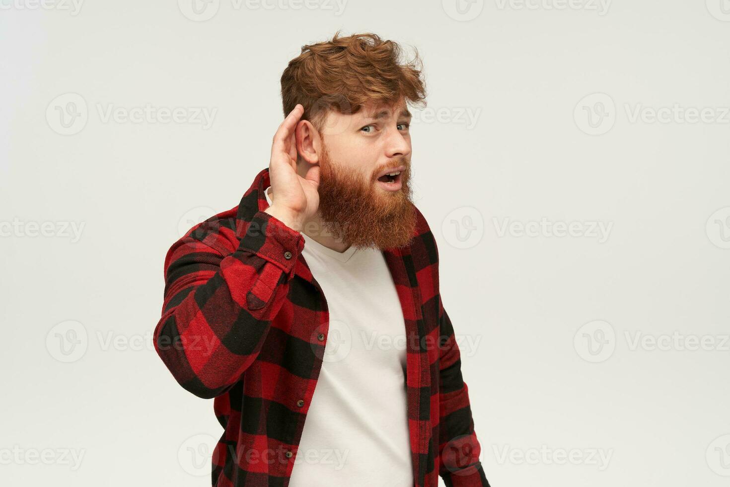 Young bearded hipster male with big red beard, turn his ear into camera, trying to hear something. Isolated over white background. photo