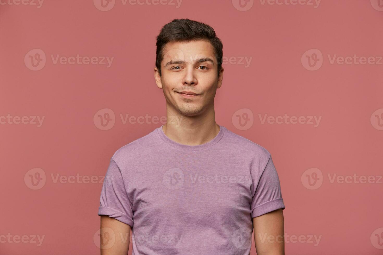 Portrait of handsome young man wears in blank t-shirt, looks at the camera with with a grin and happy expression, stands over pink background. photo