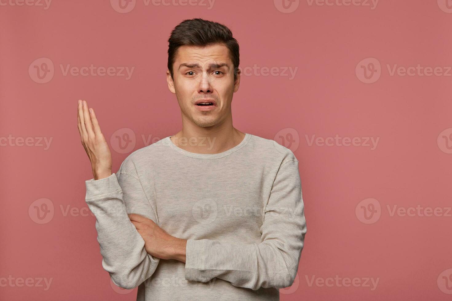 Portrait of young indigant guy wears in blank long sleeve, looks at the camera with surprised expression, looks shocked, isolated over pink background. photo