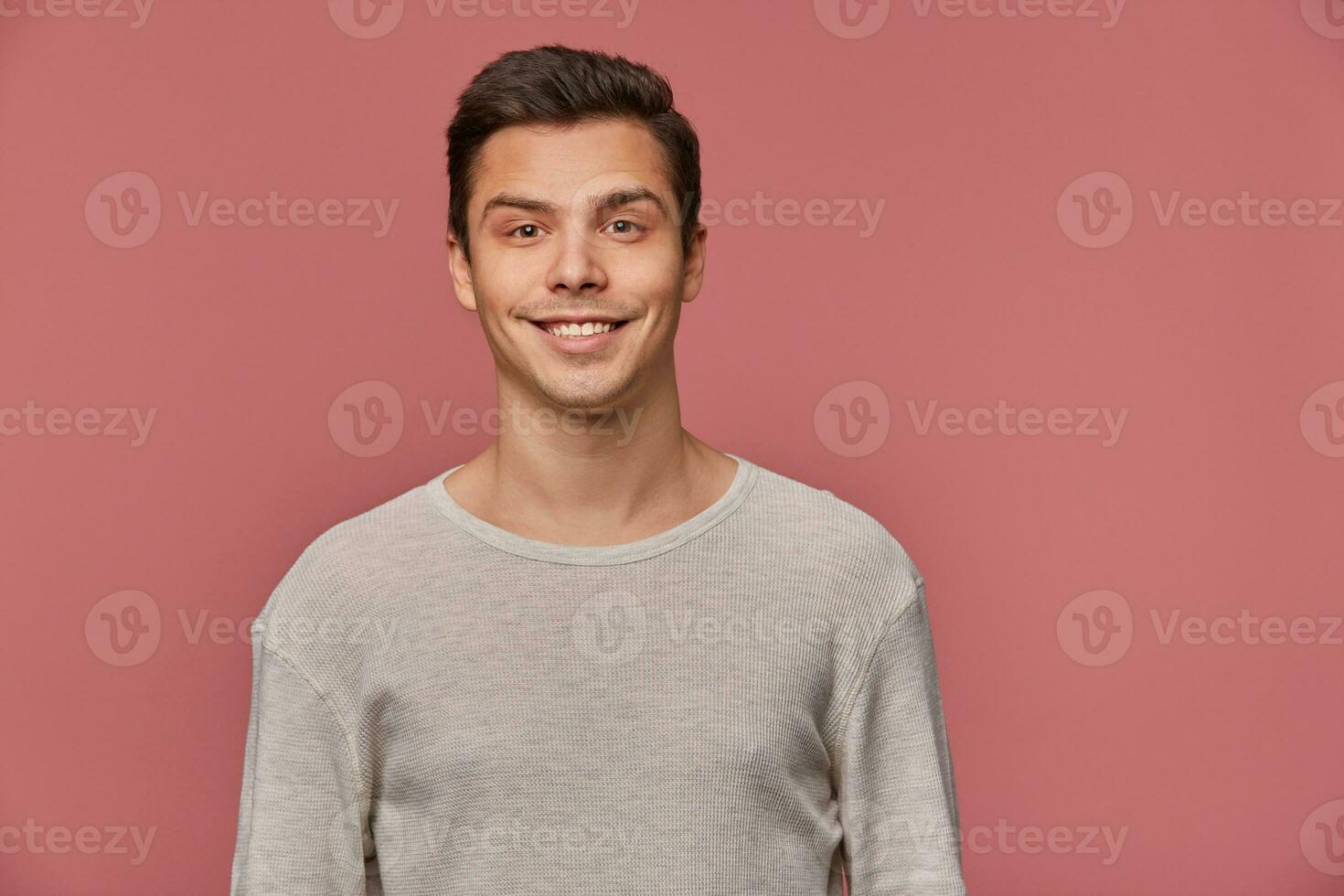 Photo of smiling handsome young guy wears in blank long sleeve, looks cheerful and glad, looks at the camera with happy expression, stands over pink background and smiling.