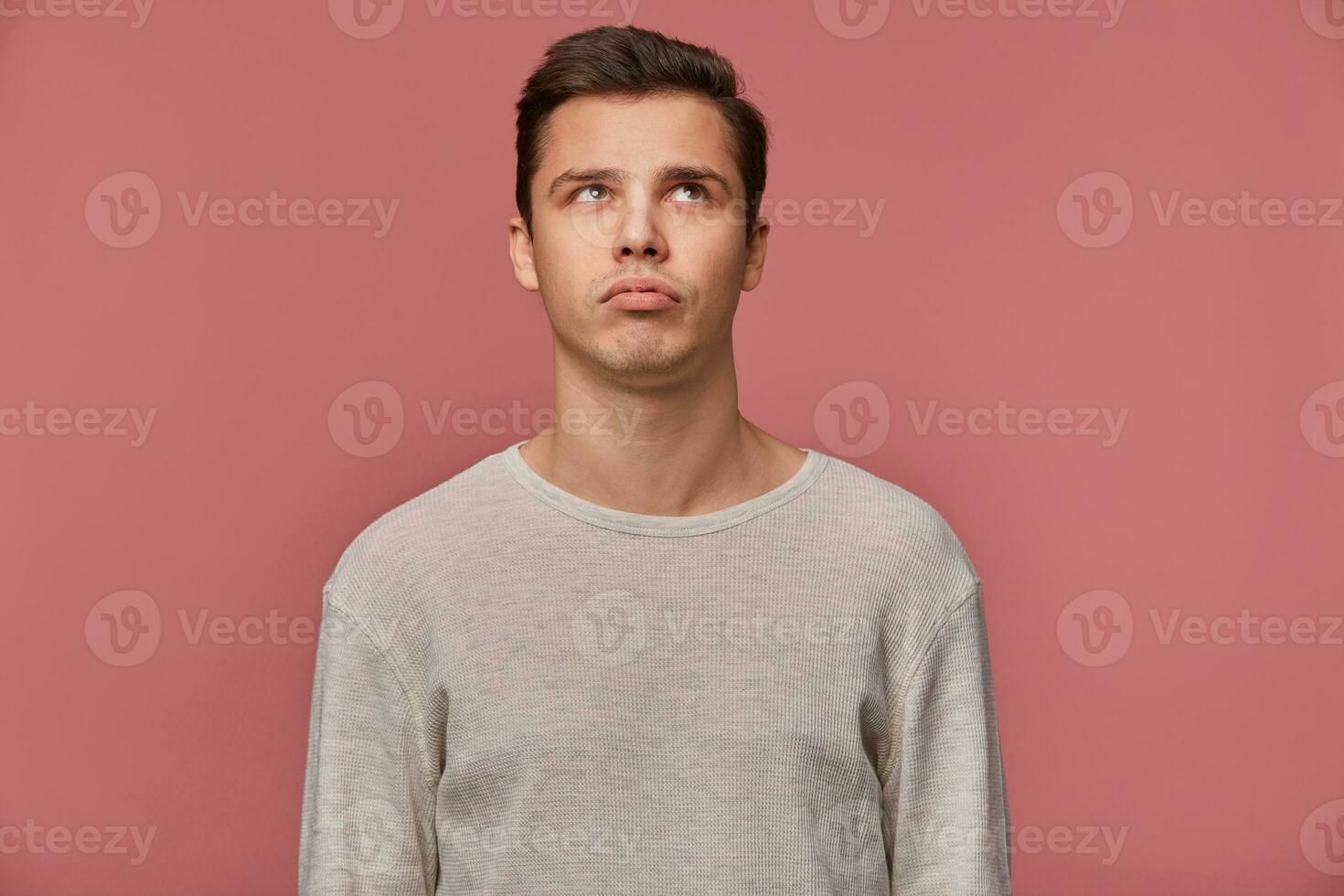 Young handsome thinking guy wears in checkered shirt, looks and away touches chin, looks bored, isolated over pink background. photo