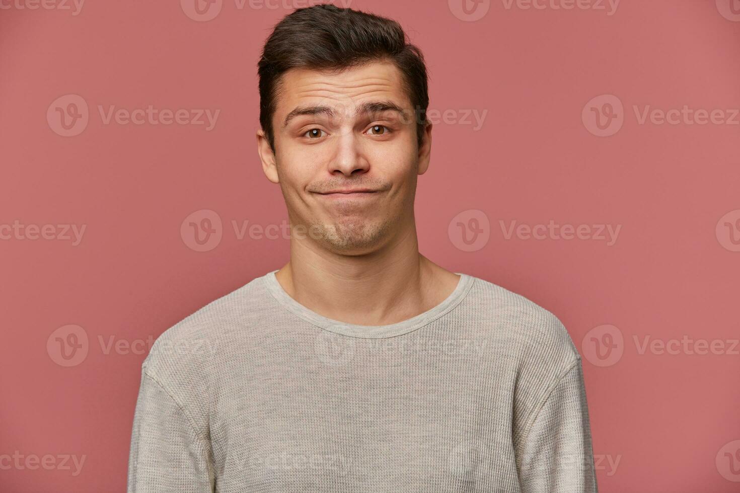 Portrait of handsome young sad man wears in blank t-shirt, looks at the camera with with mistrust, stands over pink background. photo