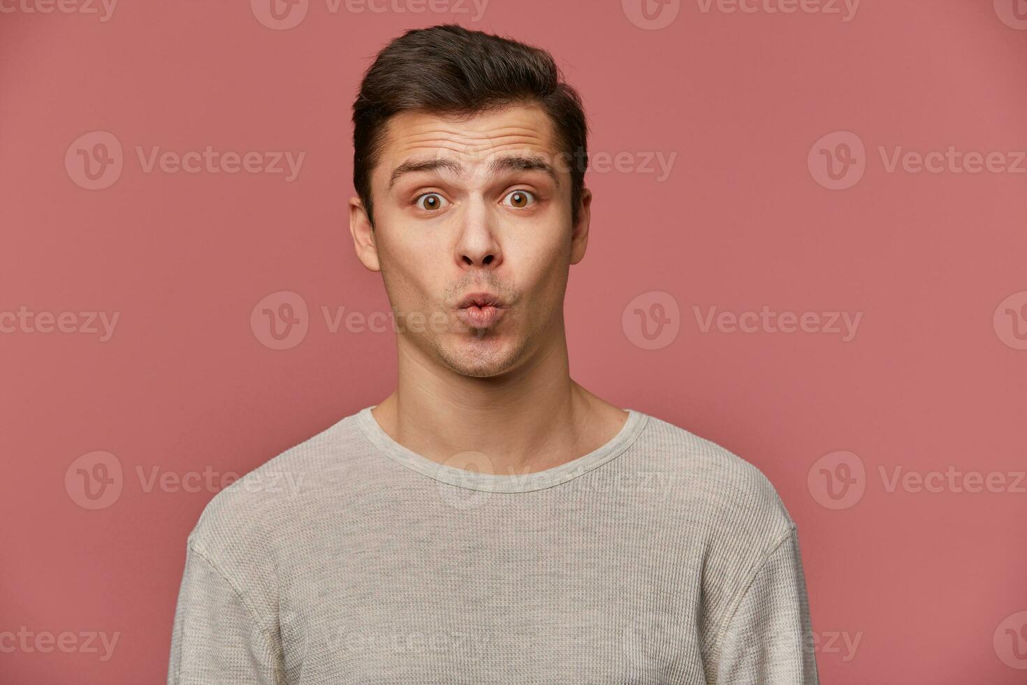 Portrait of handsome young cheerful man wears in blank long sleeve, looks at the camera with happy expressions,sens kiss, stands over pink background. photo