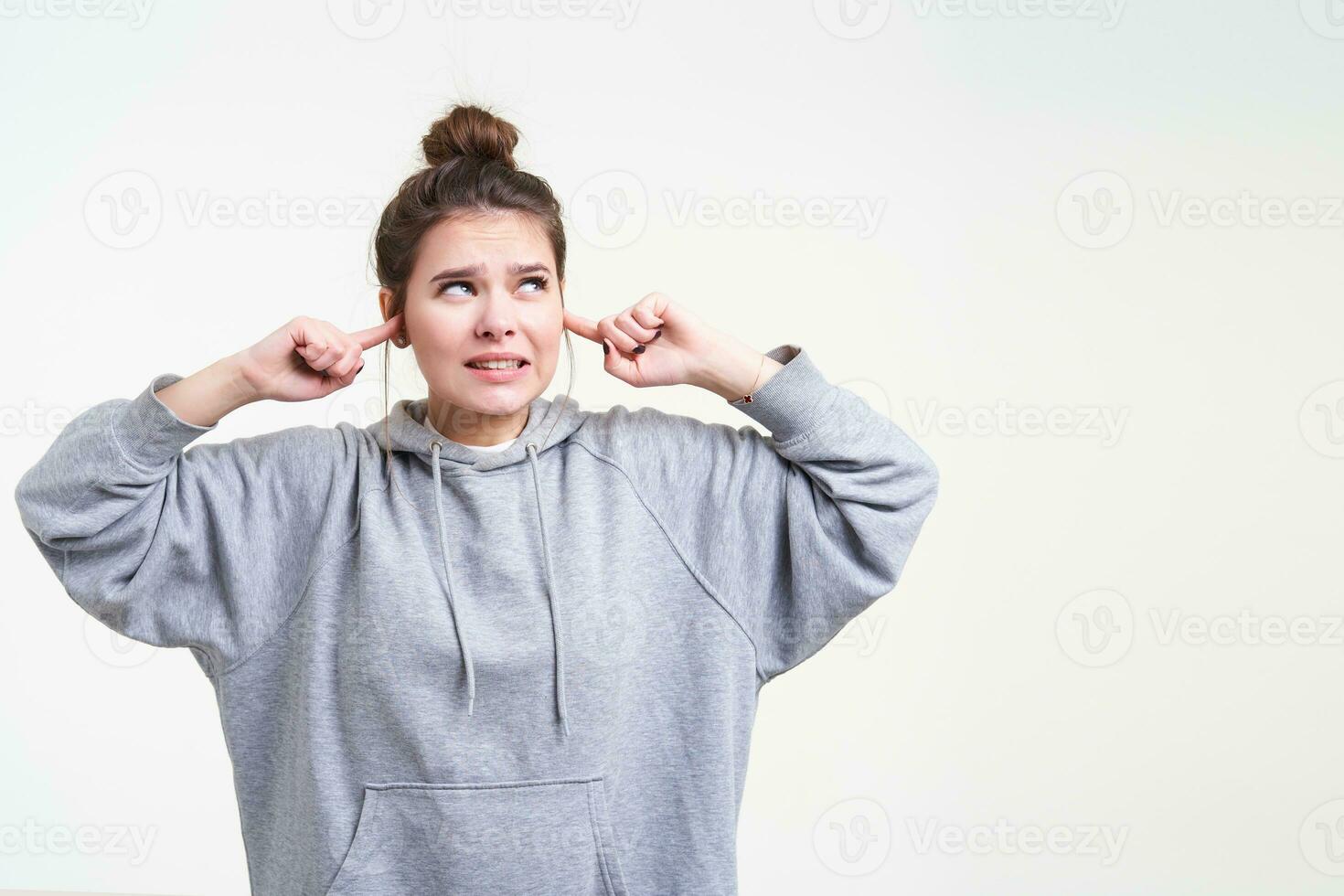 Displeased young pretty long haired lady with natural makeup frowning her face and covering ears while trying to avoid loud sounds, isolated over white background photo