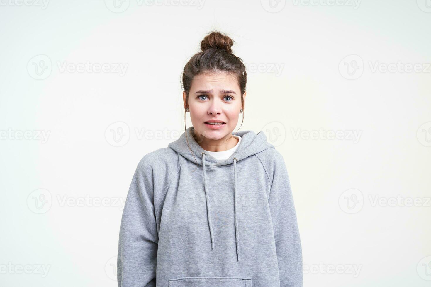 Puzzled young blue-eyed long haired woman with casual hairstyle looking confusedly at camera while standing against white background with hands down photo