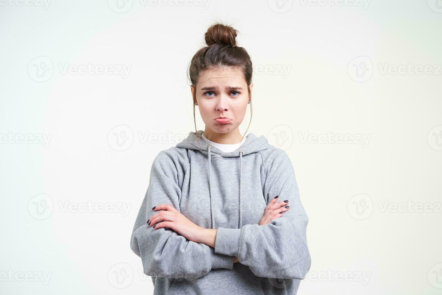 Unhappy young blue-eyed brown haired woman with natural makeup pouting her lips while looking sadly at camera, isolated over white background with crossed arms photo