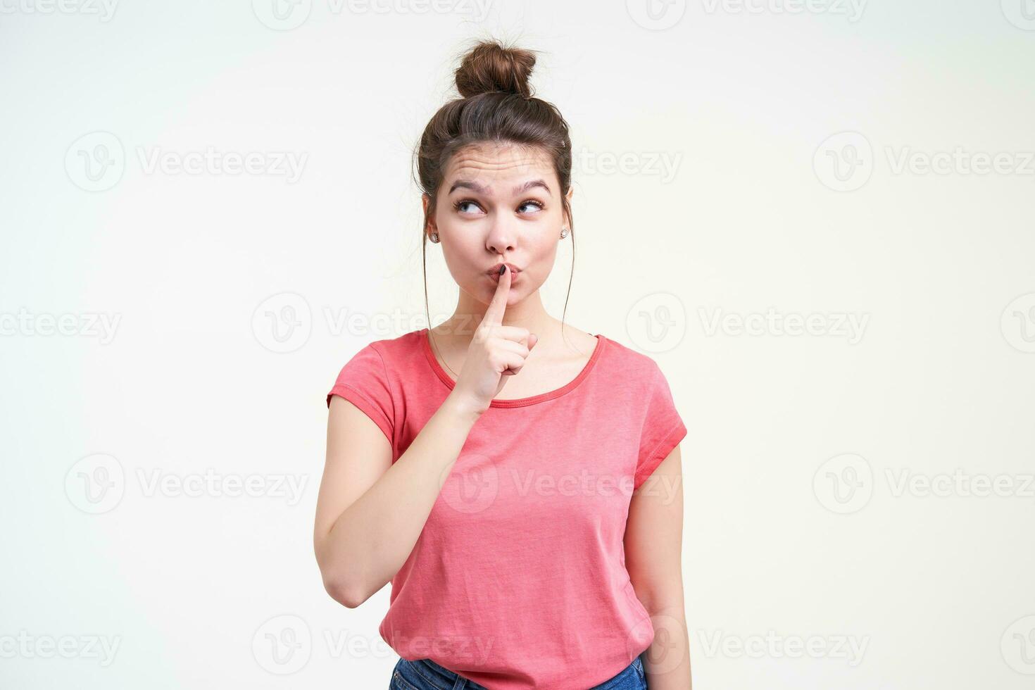 Studio shot of positive young attractive woman with casual hairstyle raising hand with hush gesture while going to tell something secret, isolated over white background photo