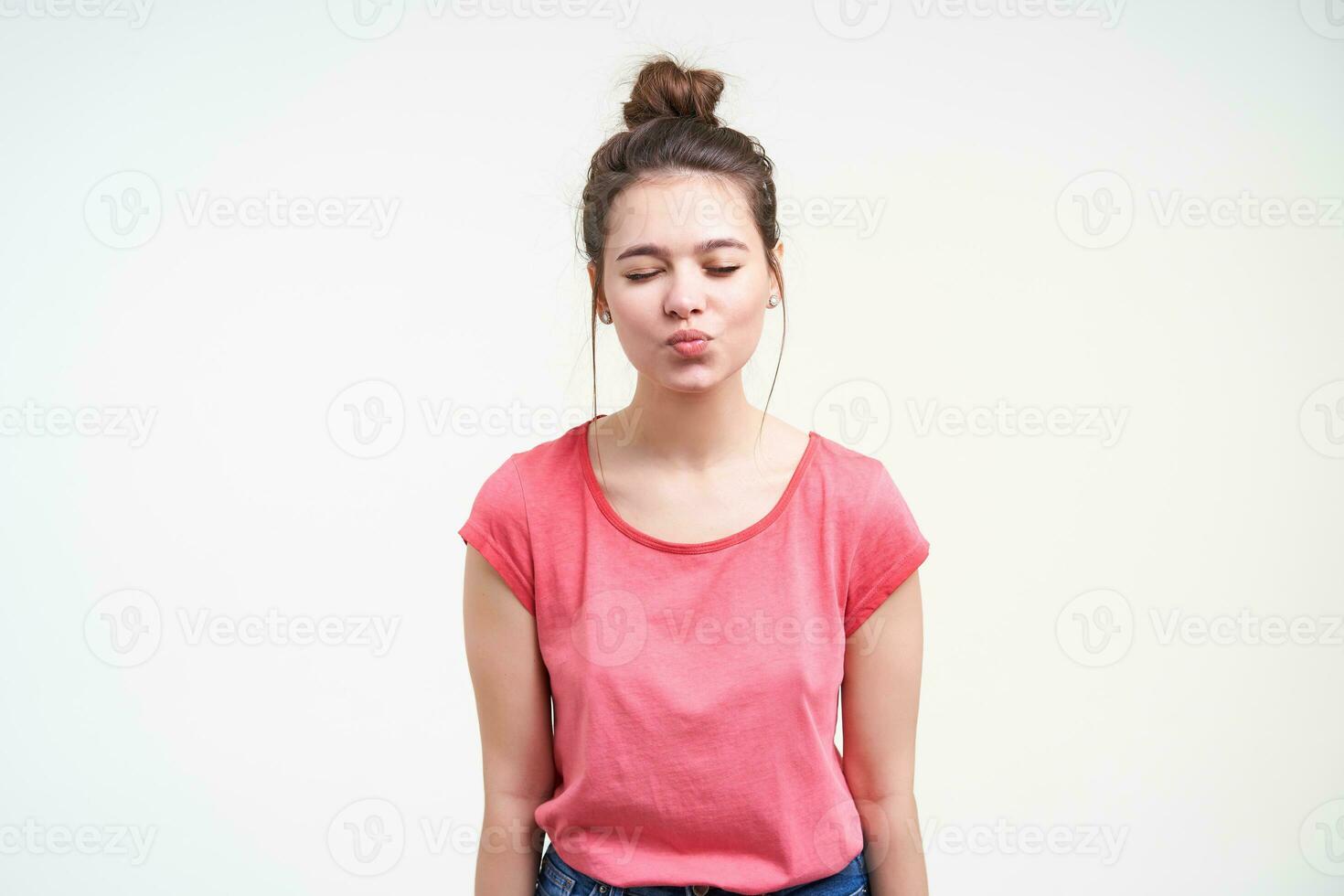 Good looking young charming brown haired woman with natural makeup keeping her eyes closed while folding lips in air kiss, isolated over white background photo