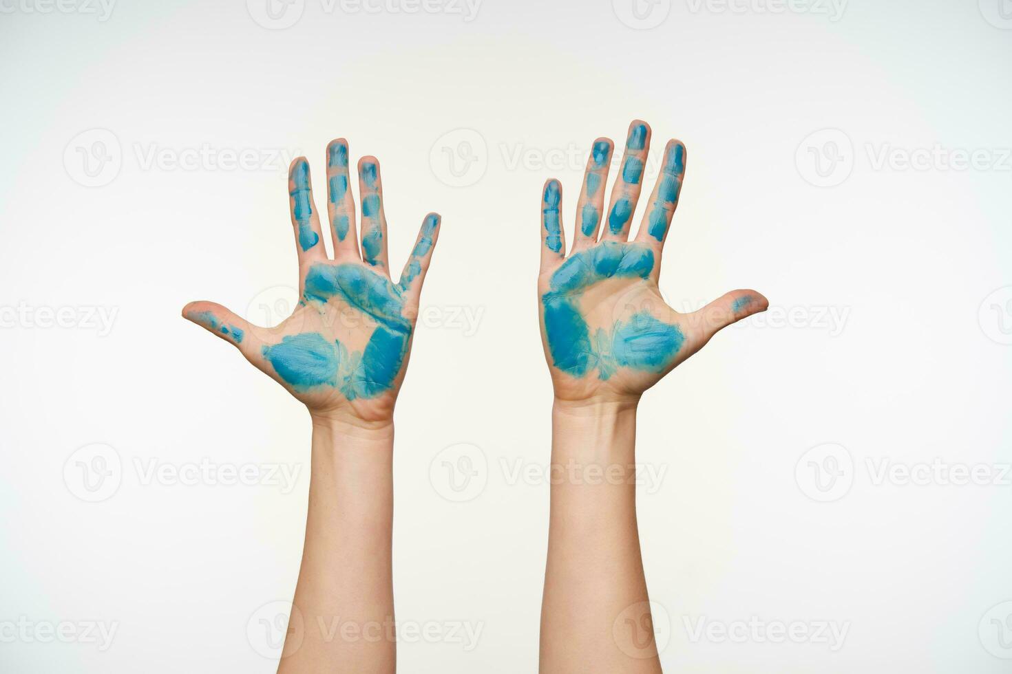 Indoor shot of painted young woman's hands being raised while showing palms with all fingers apart, isolated over white background. Human gesturing concept photo