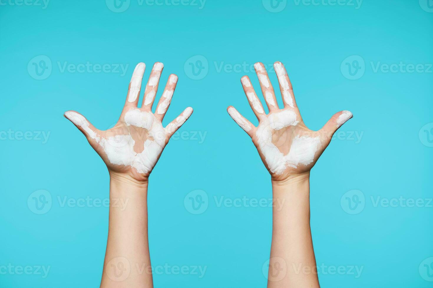 Studio photo of dirty raised woman's hand with white paint on it isolated against blue background, all fingers being separately from each other