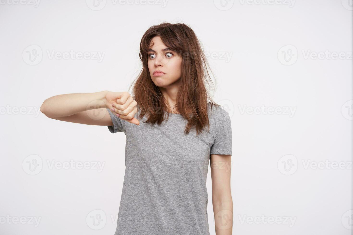Shocked young pretty brunette female rounding amazedly her blue eyes while checking time, being late because she overslept, isolated over white background photo