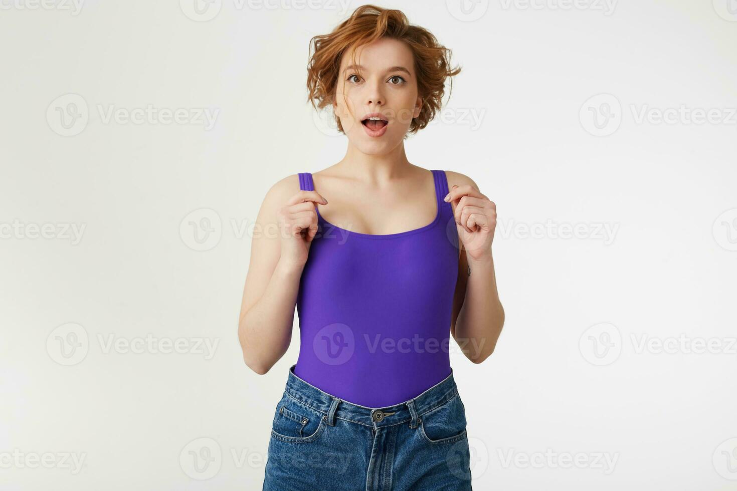 Young surprised attractive short-haired girl, wearing a purple jersey, looking at the camera with open eyes and mouth isolated over white wall. photo