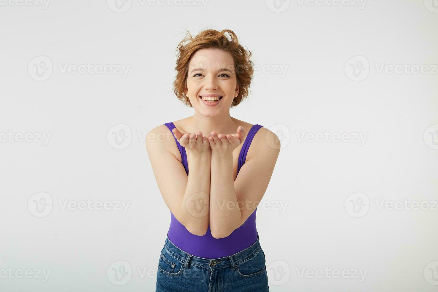 Portrait of happy cheerful young nice short-haired lady, broadly smiling, shows something in his palms, stands over white wall. photo