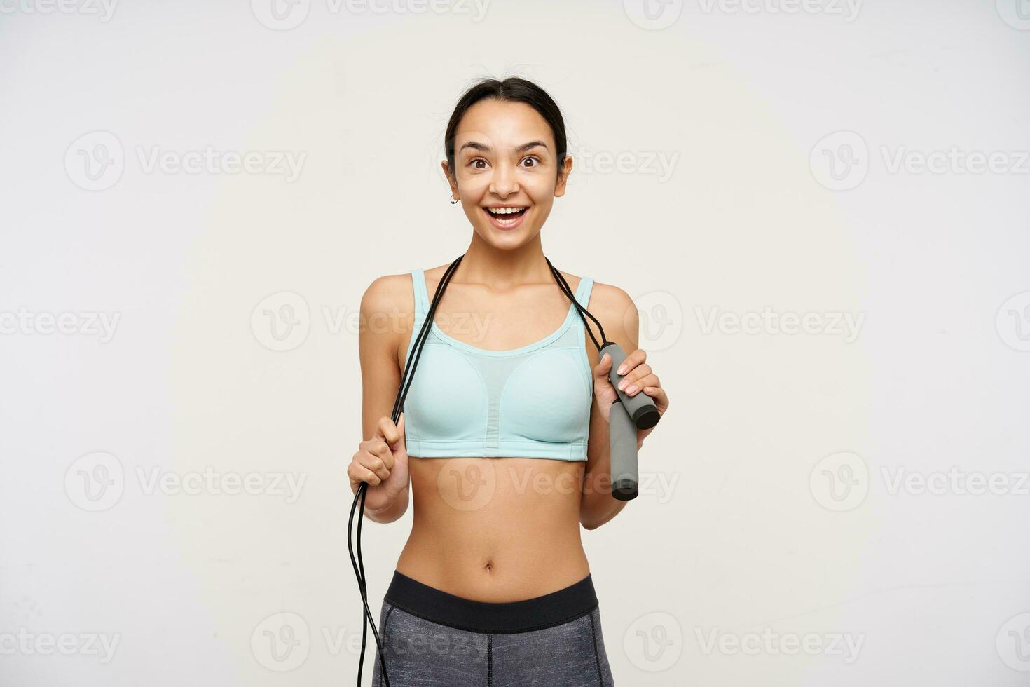 retrato de atractivo, deportivo asiático niña con oscuro largo cabello. vistiendo ropa de deporte y participación un saltar cuerda terminado su cuello. acecho a el cámara con grande sonrisa, aislado terminado blanco antecedentes foto