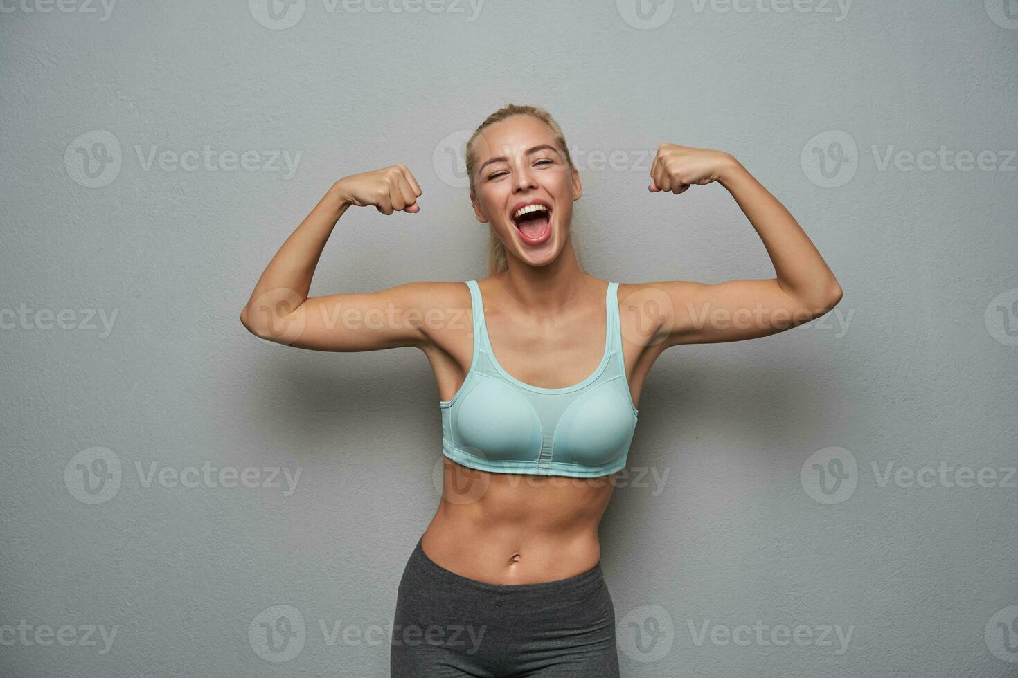 Overjoyed pretty blonde lady in good physical form posing over light grey background in mint top photo