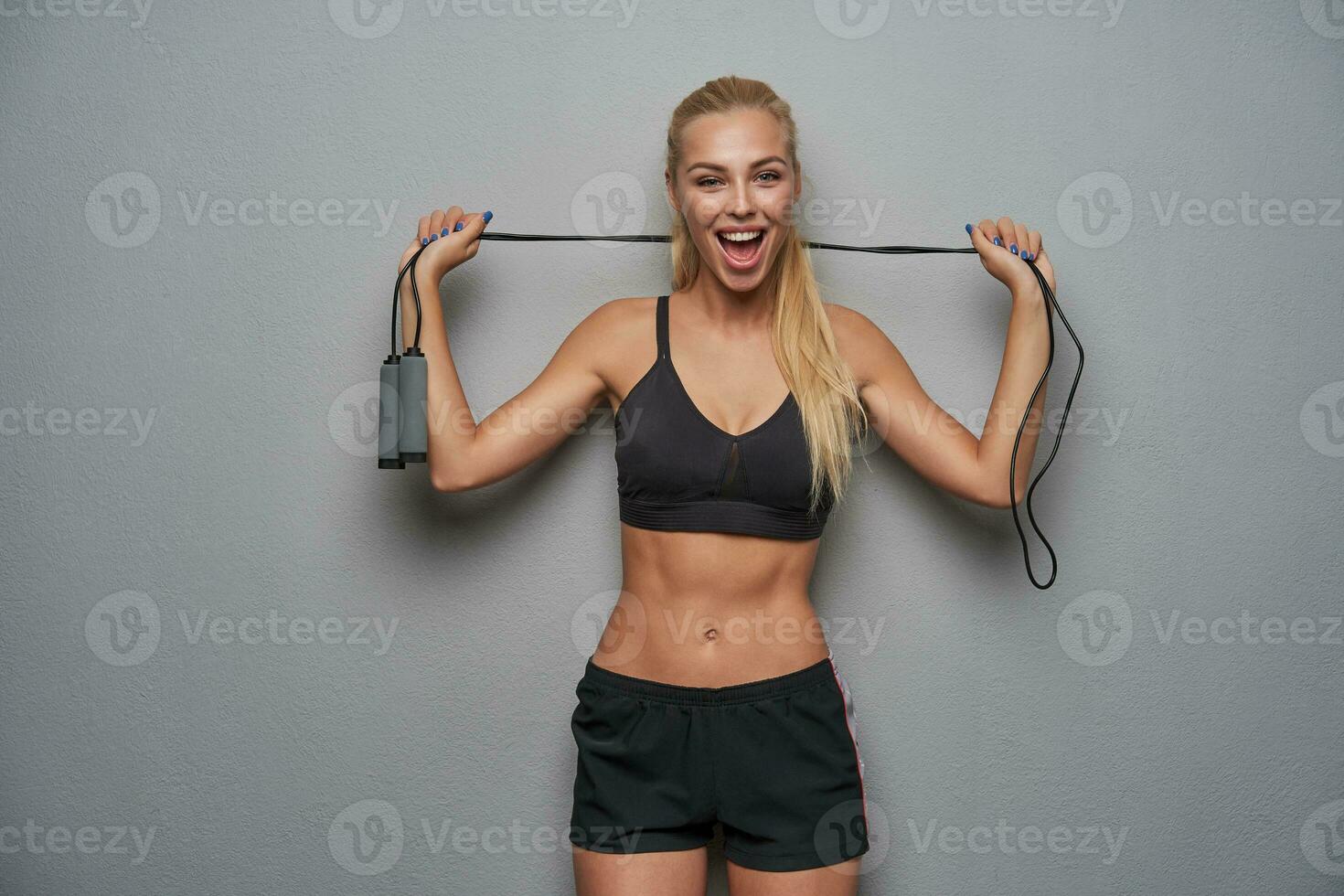 Joyful lovely young sporty blonde female with ponytail hairstyle keeping jump rope photo