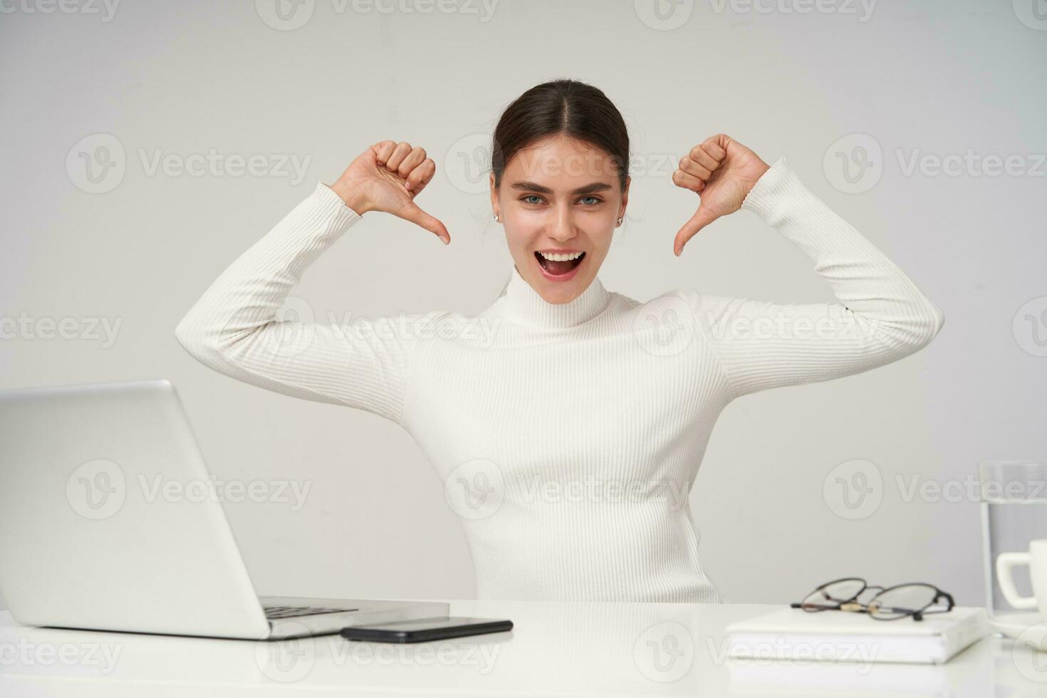 Excited young pretty dark haired woman showing on herself with raised hands and looking joyfully at camera with wide mouth opened, isolated over white background in formal clothes photo