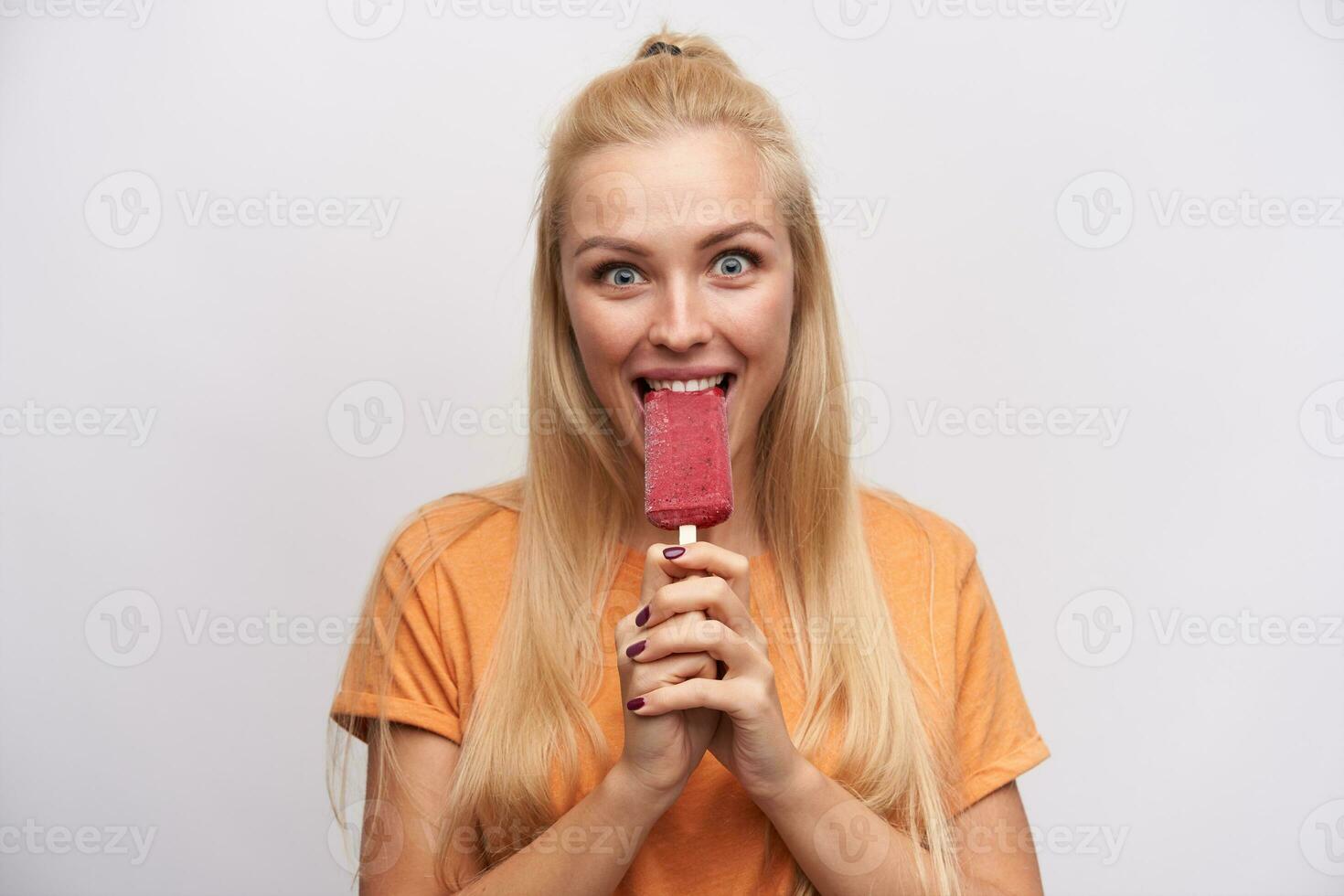 emocionado de ojos azules bonito joven largo peludo rubia dama alegría acerca de sabroso helado ella es saboreo y mirando asombrado a cámara, en pie en contra blanco antecedentes foto