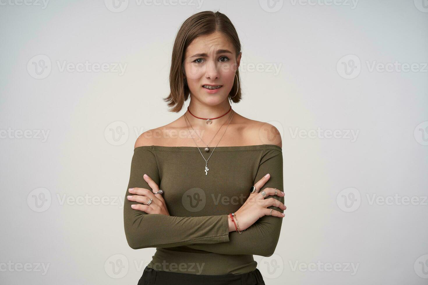 Bewildered young short haired brunette female crossing her hands on chest while looking confusedly at camera, isolated over white background in casual clothes photo