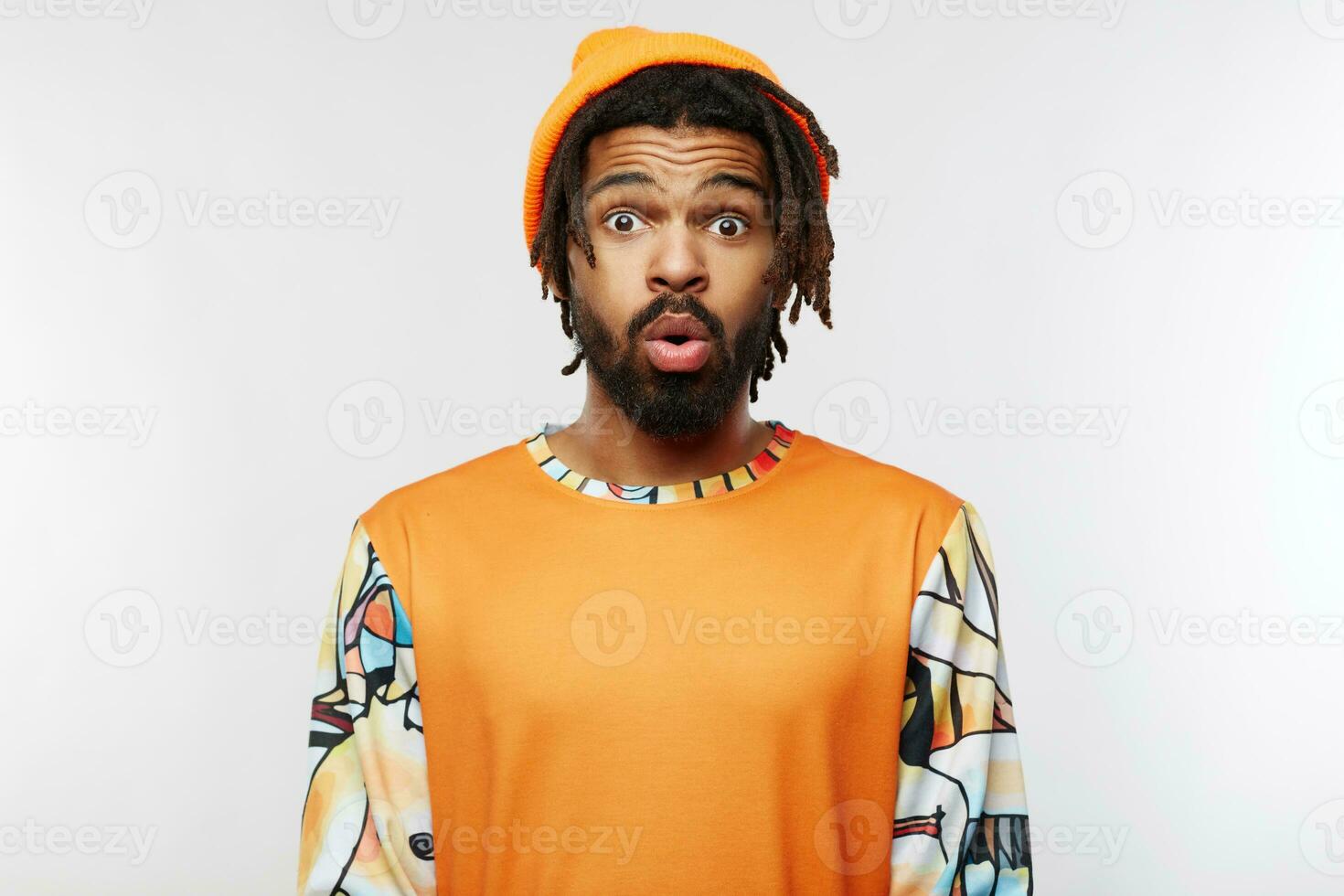 Amazed young brown-eyed brunette male raising surprisedly eyebrows while looking wonderingly at camera with wide eyes opened, isolated over white background photo