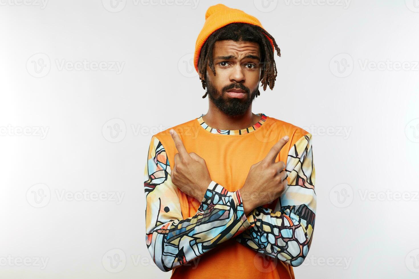 Puzzled young dark skinned brunette male keeping his lips folded while frowning eyebrows and showing in different sides with index fingers, isolated over white background photo