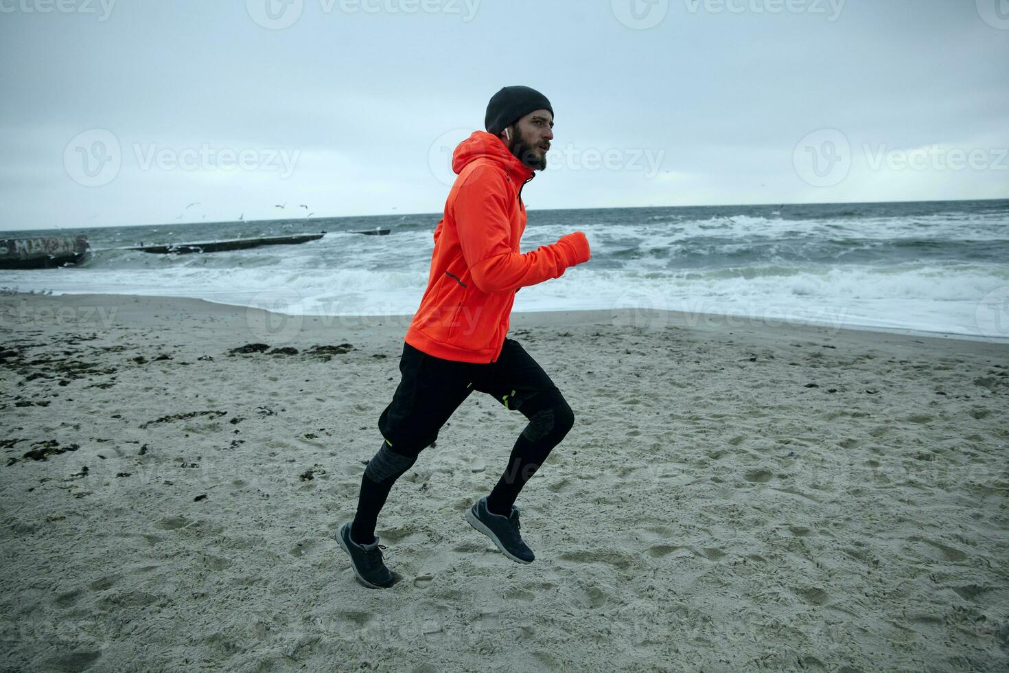 Side view of young handsome active bearded man enjoying morning jugging on fresh cold weather, listening to favourite music list while doing morning exercises outdoor photo