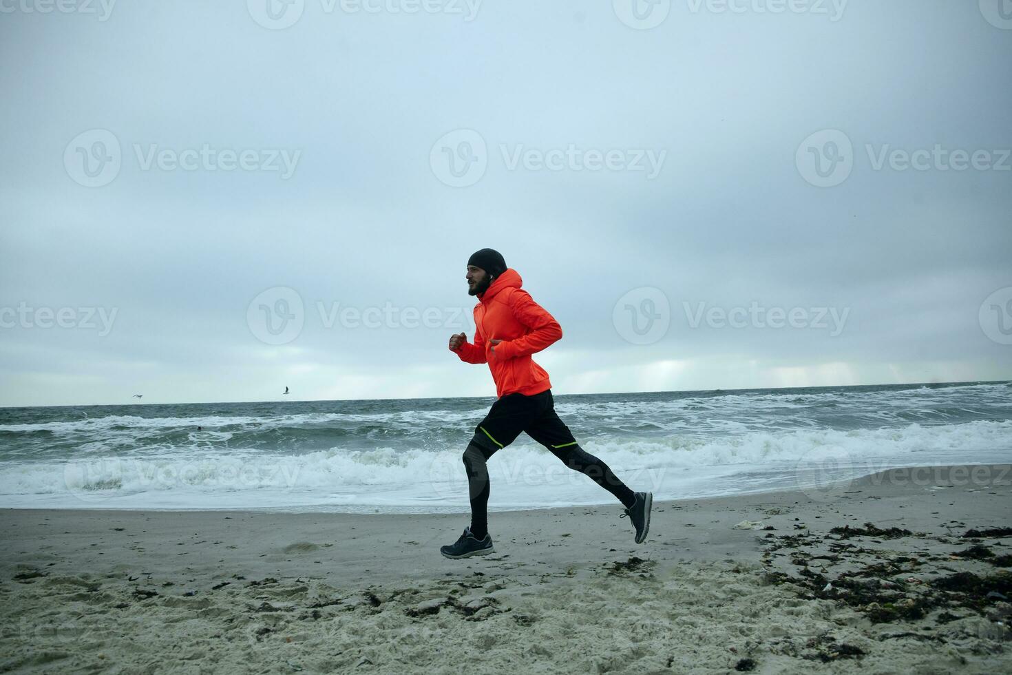 Side view of young active brunette bearded male dressed in warm sporty clothes starting day from morning jog. Male fitness jogging training wellness concept photo