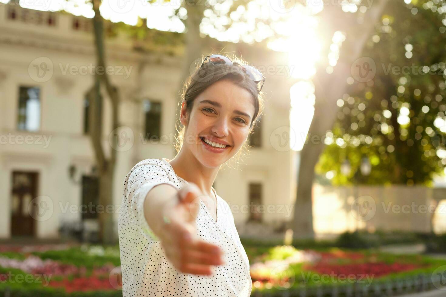 hermosa joven oscuro peludo morena de ojos marrones hembra levantamiento mano en Bienvenido gesto mientras mirando felizmente a cámara y sonriente en términos generales, vistiendo Gafas de sol en su cabeza foto