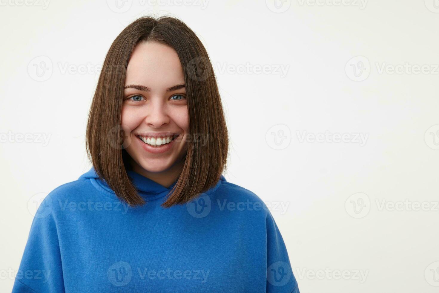 Indoor photo of young happy brown haired woman with short haircut showing her perfect white teeth while smiling cheerfully, isolated over white background