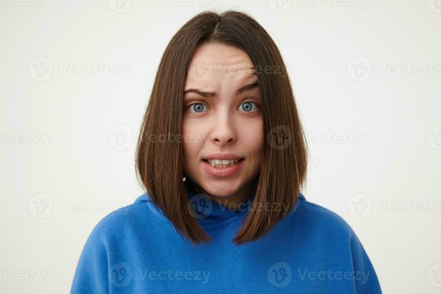 Portrair of young lovely short haired blue-eyed woman without makeup raising confusedly eyebrow while looking at camera, isolated over white background photo