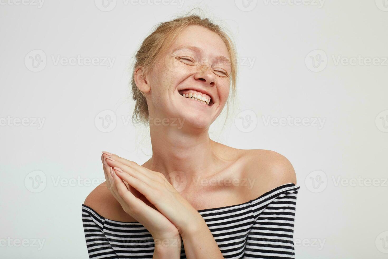 satisfecho joven atractivo pelirrojo hembra con natural maquillaje acuerdo elevado palmas juntos y sonriente alegremente con cerrado ojos, en pie en contra blanco antecedentes foto