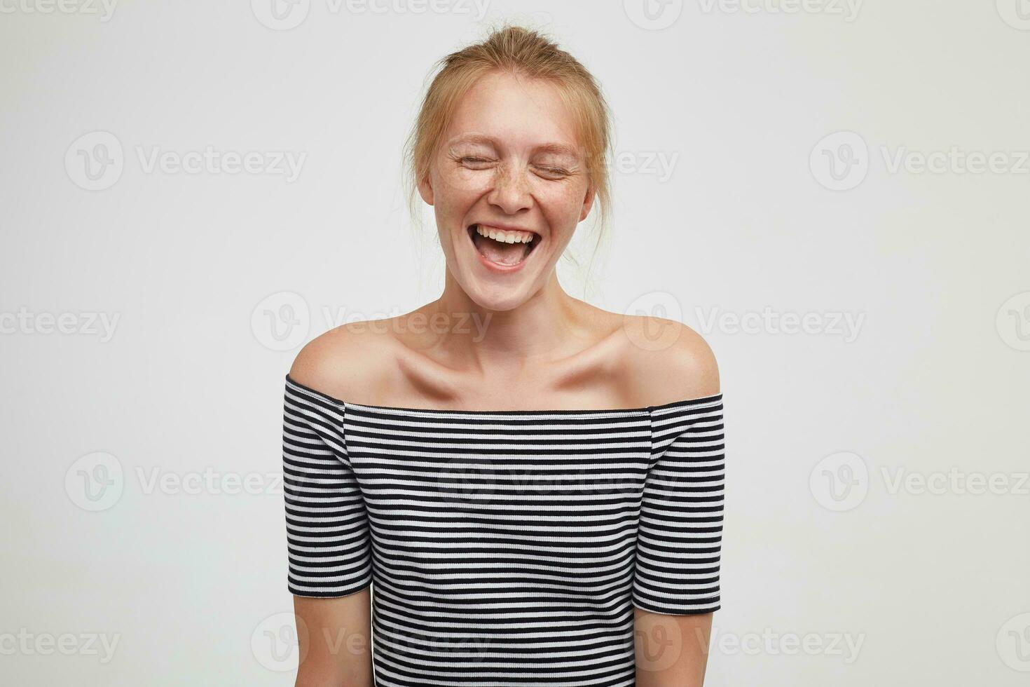 Good looking overjoyed young lovely redhead female keeping her eyes closed while laughing happily, wearing casual clothes while posing over white background with hands down photo