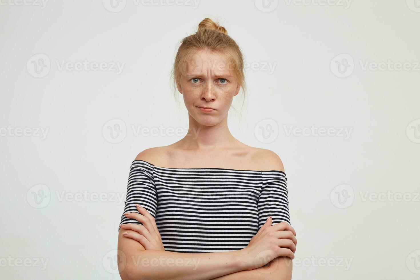 Severe young attractive redhead woman with natural makeup crossing hands on her chest and frowning her eyebrows while looking confusedly at camera, isolated over white background photo