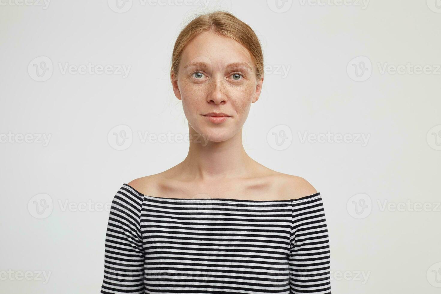 Portrait of young charming redhead lady with natural makeup looking at camera with calm face and keeping her lips folded, isolated over white background photo