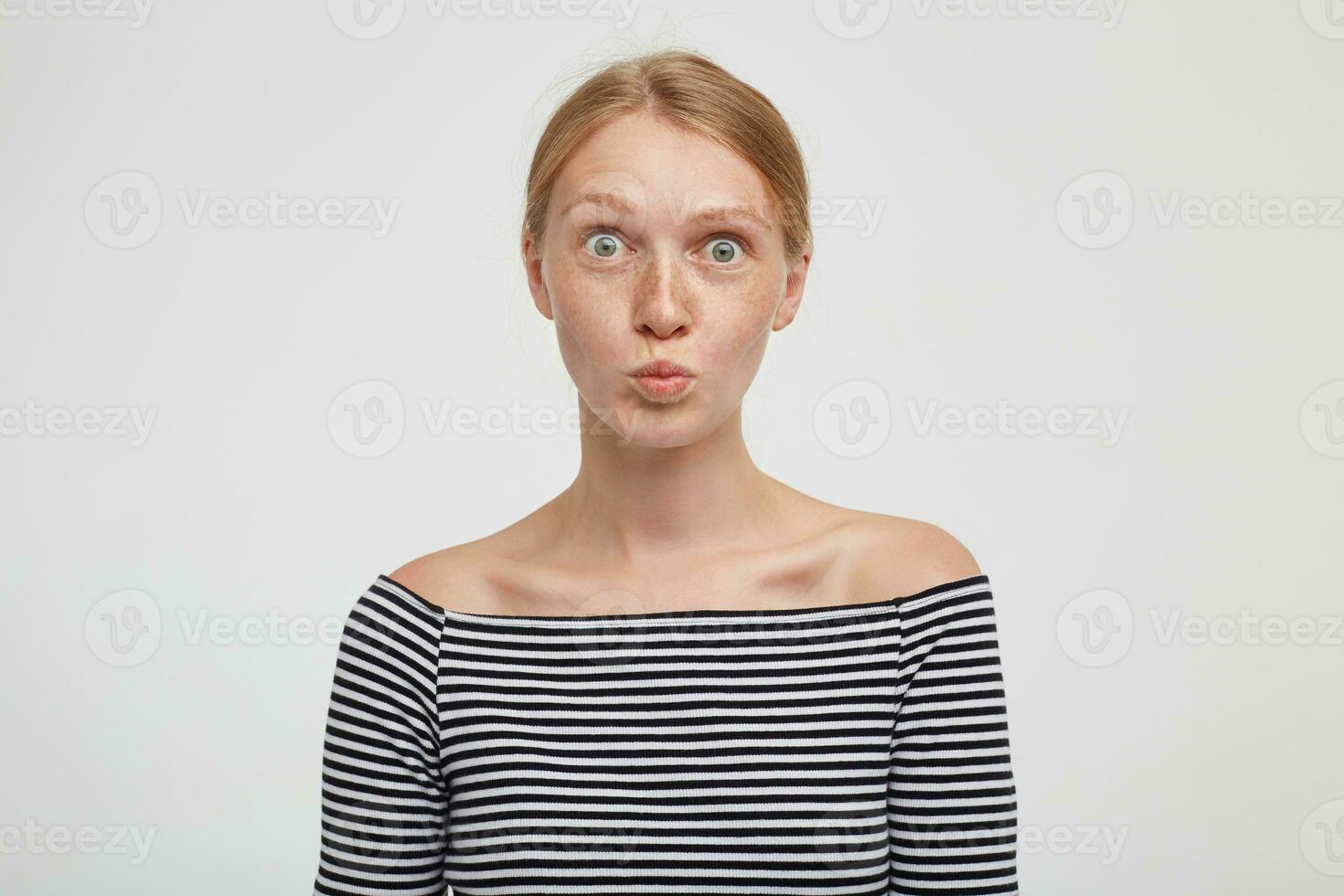 sorprendido joven bonito pelirrojo hembra con natural maquillaje redondeo su verde ojos y plegable labios mientras mirando a cámara, aislado terminado blanco antecedentes foto