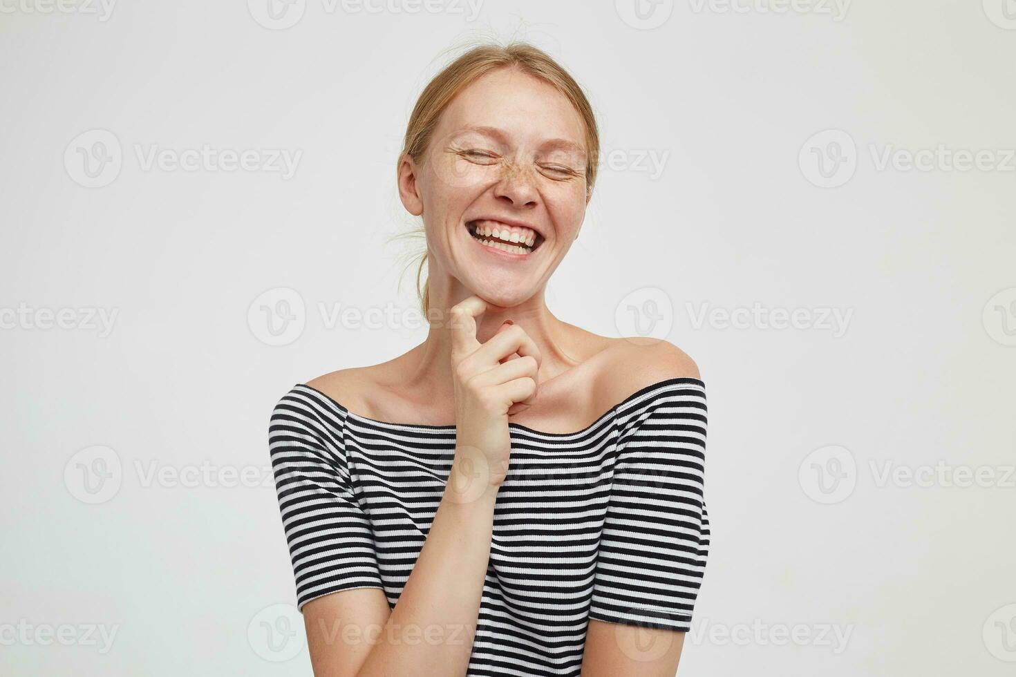 Good looking young happy redhead female with casual hairstyle laughing cheerfully with closed eyes while posing over white background in casual clothes photo