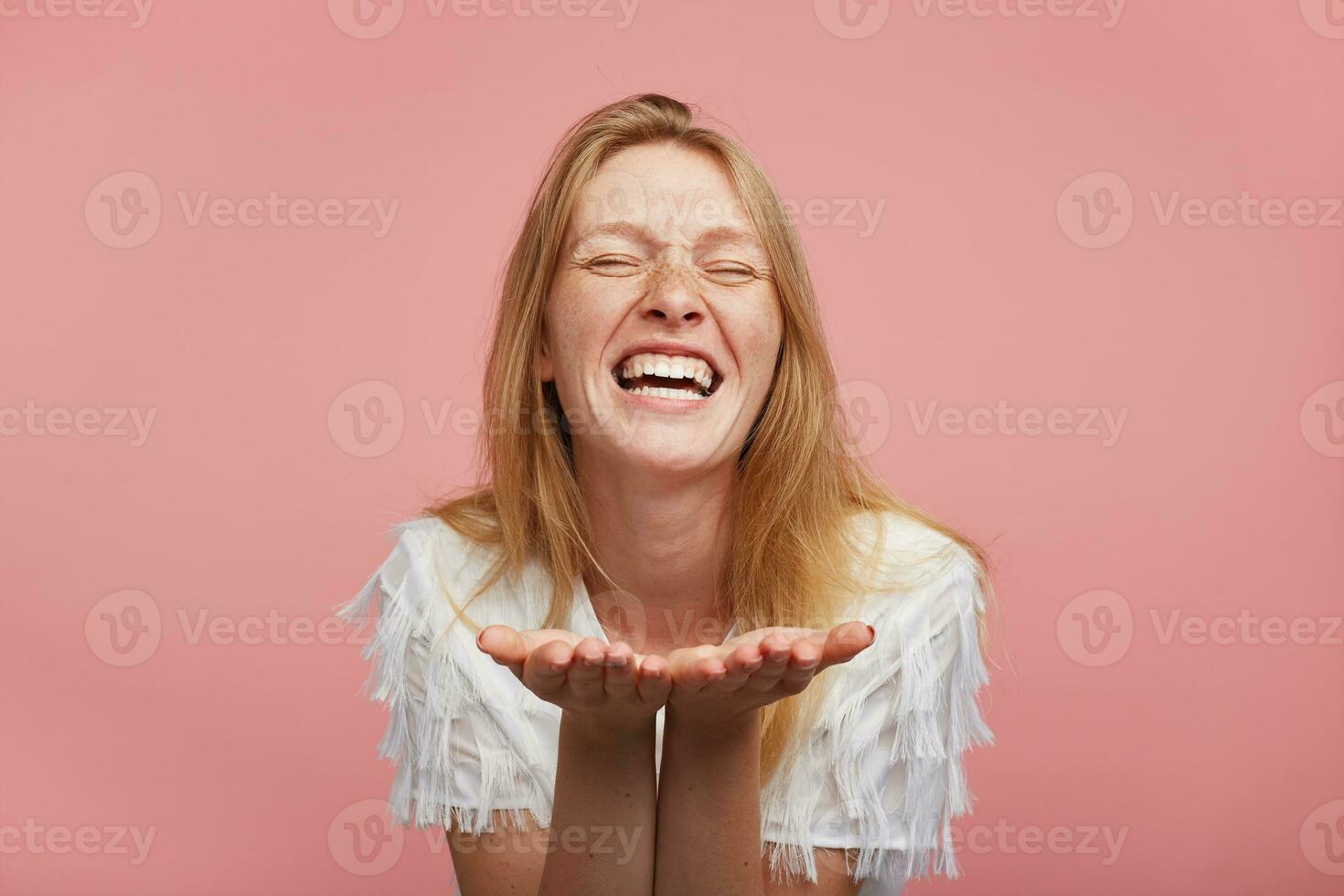 estudio foto de joven alegre hembra con astuto pelo levantamiento su palmas mientras en pie terminado rosado fondo, acuerdo ojos cerrado mientras sonriente ampliamente, siendo en alto espíritu