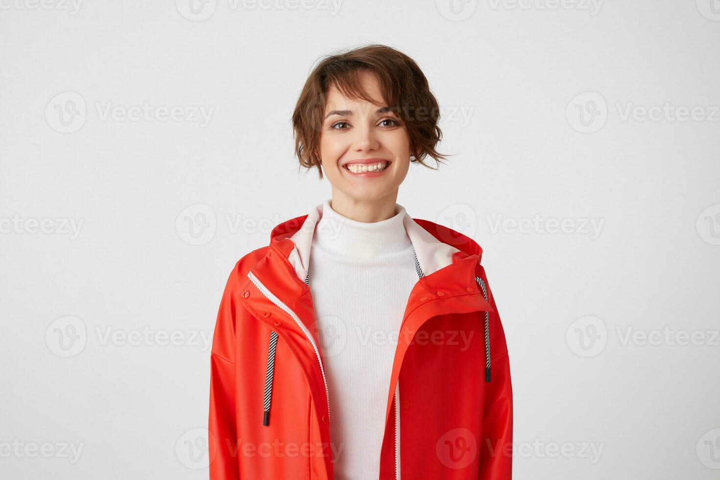 Portrait of young broadly smiling cute short haired girl dressed in white golf and red rain coat, looking at the camera with a happy expression, standing over white background. photo