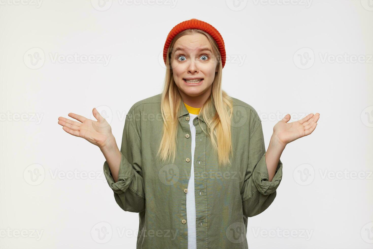 Indoor photo of young long haired white-headed lady shrugging confusedly with raised palms and grimacing her face, standing over blue background in casual wear