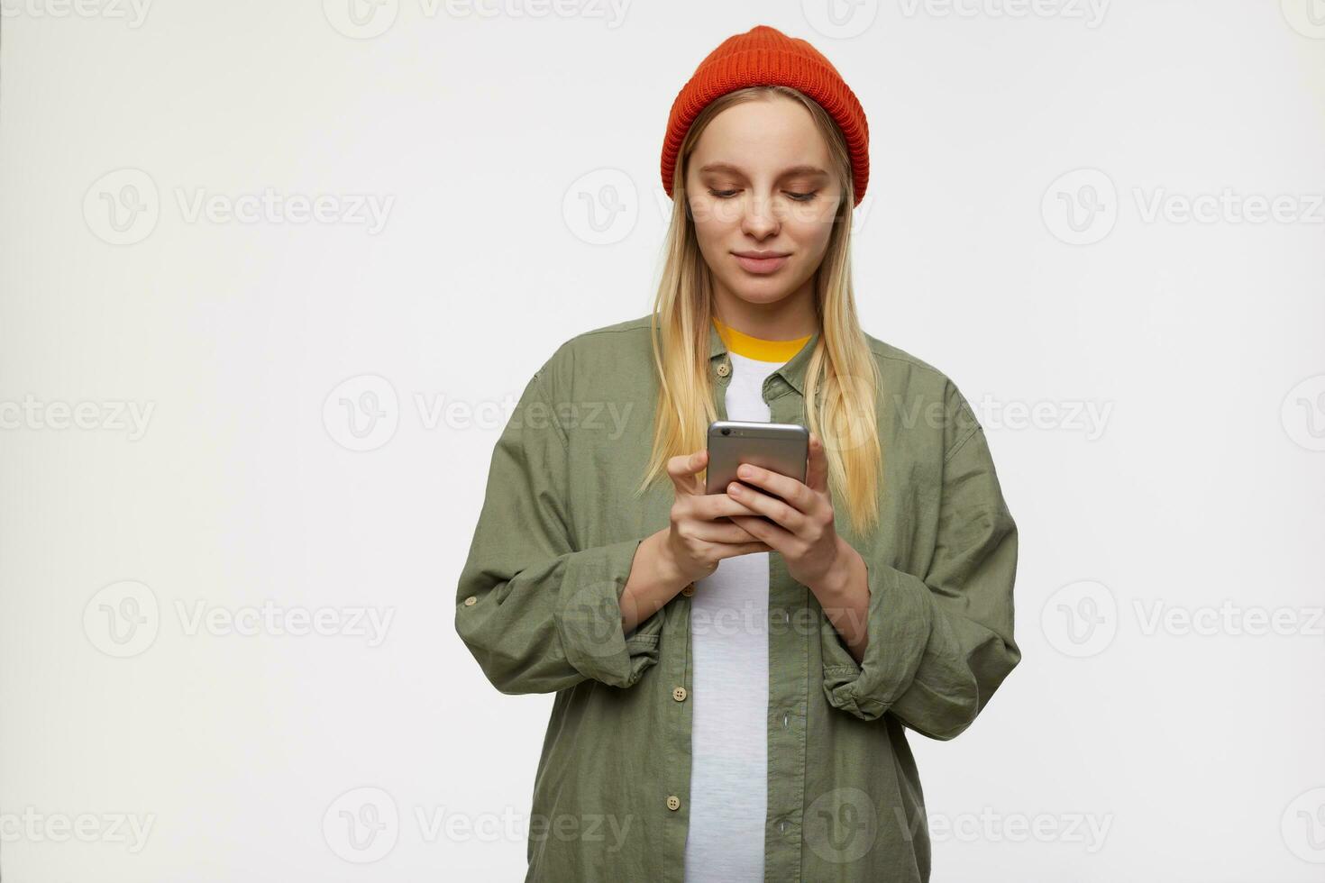 Indoor shot of young attractive long haired white-headed lady keeping mobile hand in raised hands and looking attentively on screen, standing over blue background photo
