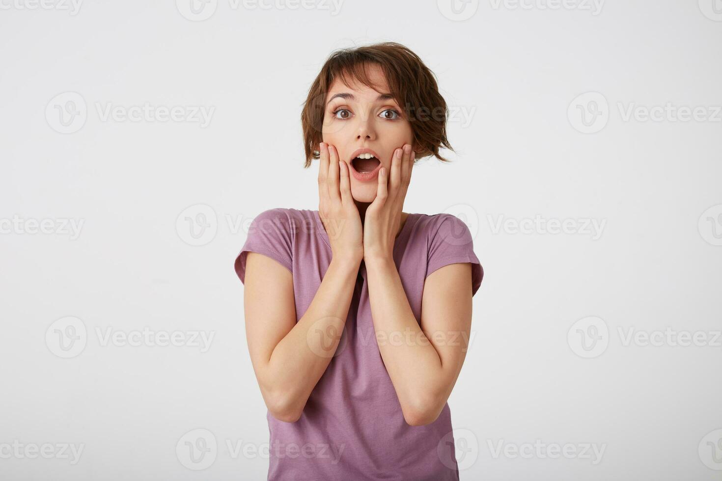 Portrait of happy amazed young attractive girl in with a surprised expression on her face, standing over white wall with wide open moth and eyed. Positive emotion concept. photo