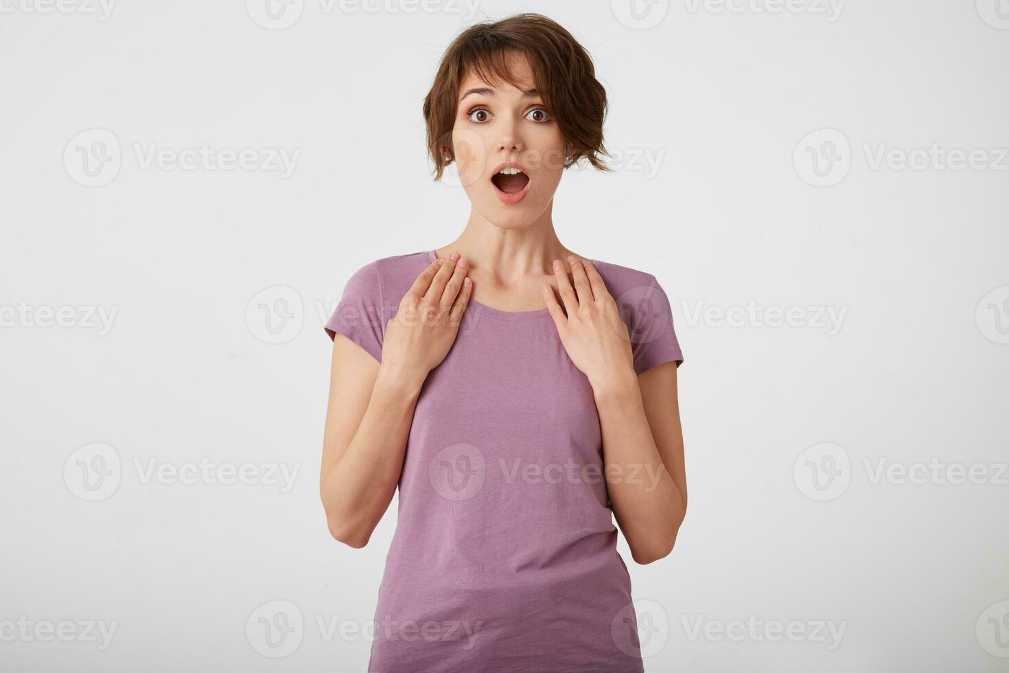 Young surprised cheerful short-haired lady in blank t-shirt, heard amazed news, stands over white background with wide open eyes and mouth. photo