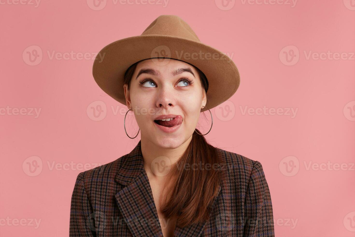 retrato de joven soñando hermosa mujer, piensa acerca de el delicioso postre y lame. mirando lejos aislado terminado rosado antecedentes. foto